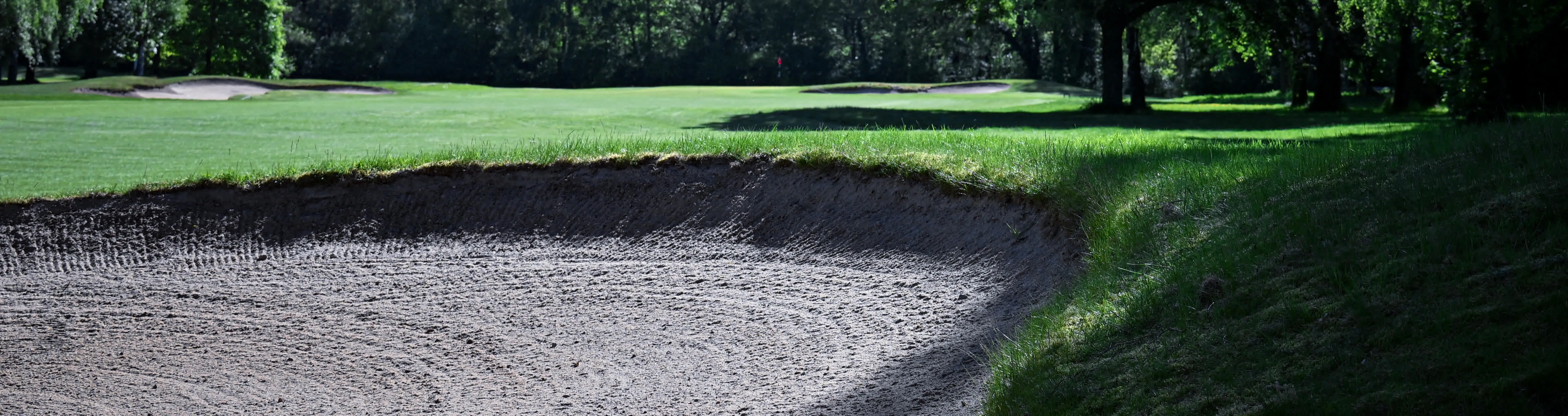 Golfplatz mit Bunker, Fairway und Fahne im Sonnenlicht